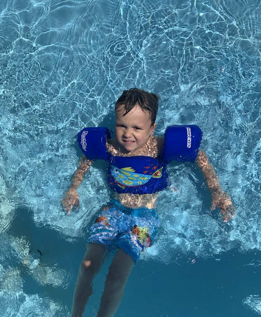 A little boy swimming in the water with blue floaties on.